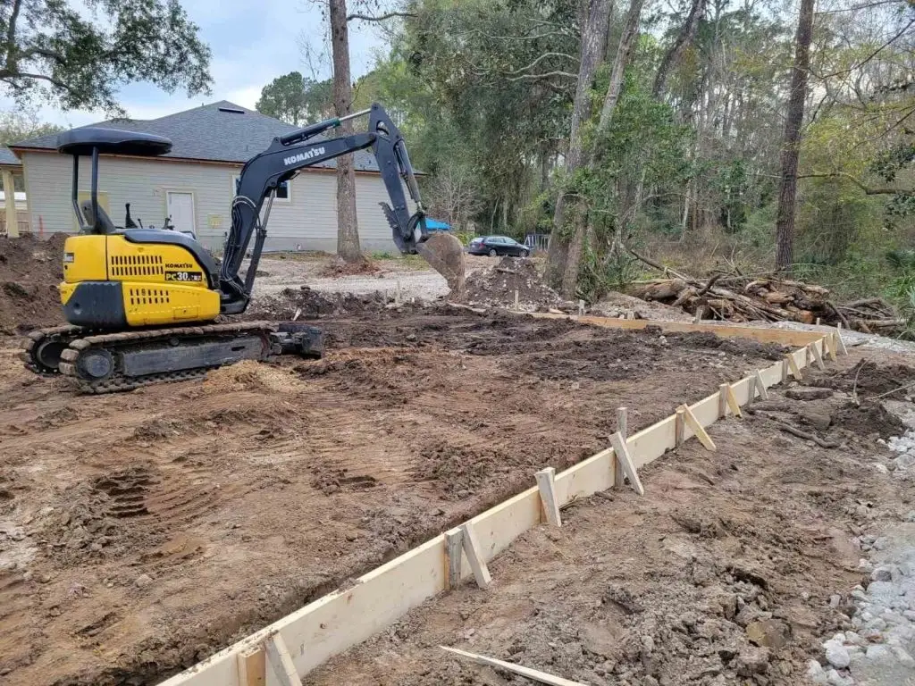 Excavation site featuring a Komatsu PC30 excavator working on soil preparation, with wooden forms in place and wooded area in the background, illustrating Arc Excavation's construction services in Jacksonville.