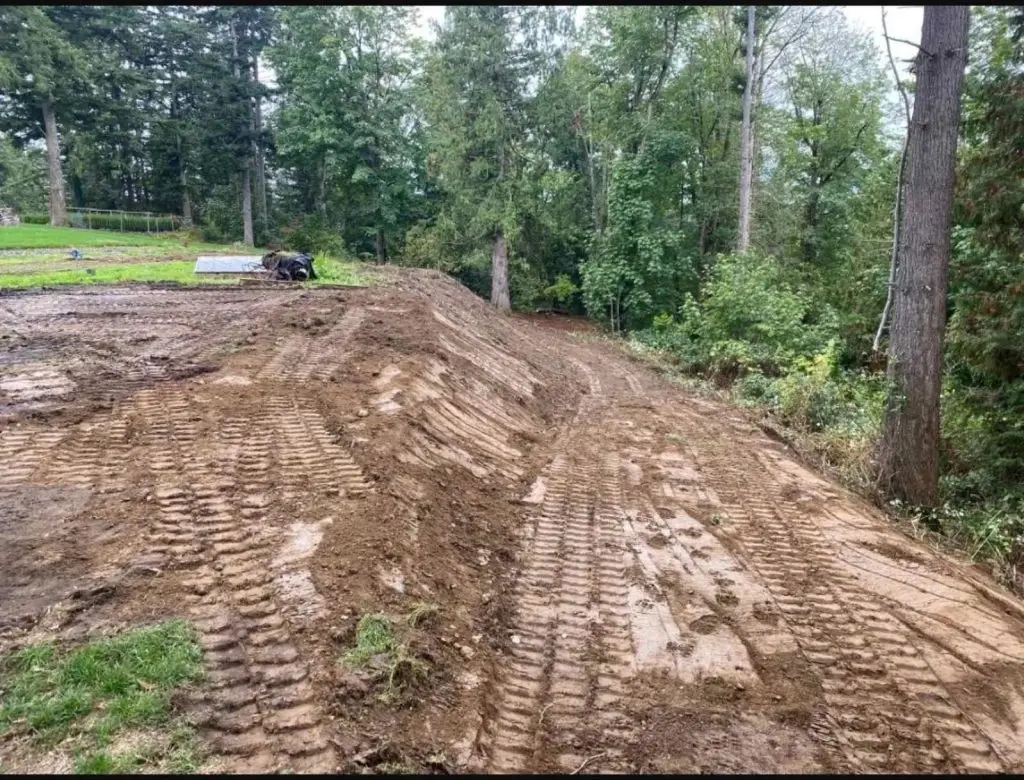 Excavated site with tire tracks, showcasing land grading and preparation for construction, surrounded by trees in a natural setting, relevant to excavation and hardscaping services in Jacksonville.