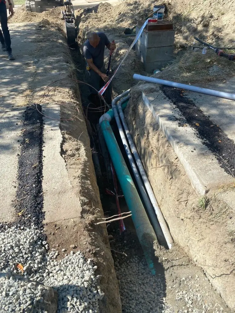 Excavation site showing a worker inspecting underground utilities in a trench, with visible pipes and construction equipment in Jacksonville, Florida.