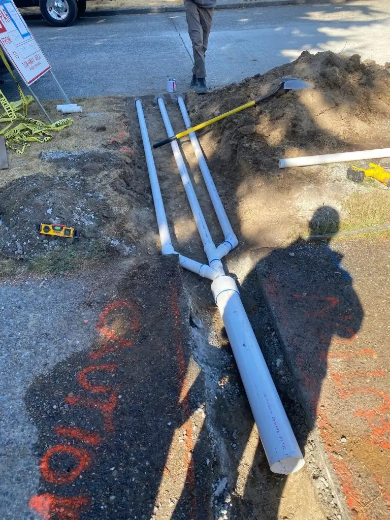 Excavation site showing installed drainage pipes, tools including a shovel and level, with caution tape and a nearby vehicle, illustrating Arc Excavation's drainage solutions in Jacksonville.