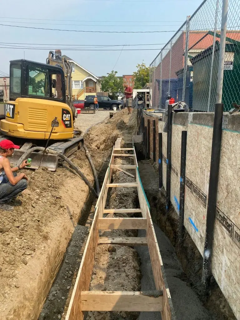 Excavation site featuring a CAT 306E excavator, workers preparing a trench with wooden supports, and surrounding construction elements, illustrating Arc Excavation's expertise in excavation and site work.