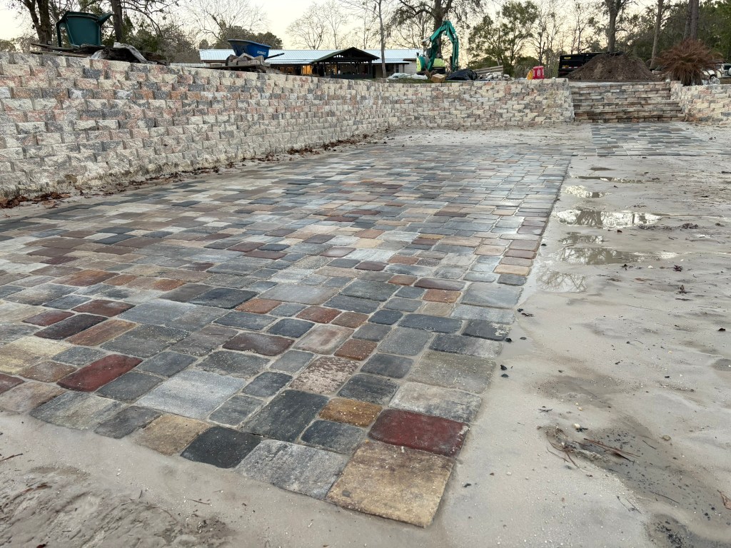 Retaining wall and paver installation featuring a multi-colored paver surface, showcasing a newly constructed outdoor space with erosion control and aesthetic appeal.