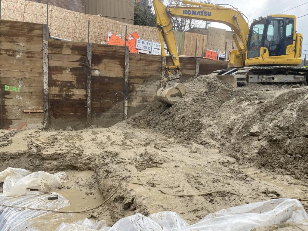 Excavator working on a construction site in Jacksonville, FL, with dirt and wooden retaining walls, illustrating professional concrete removal and site preparation services.